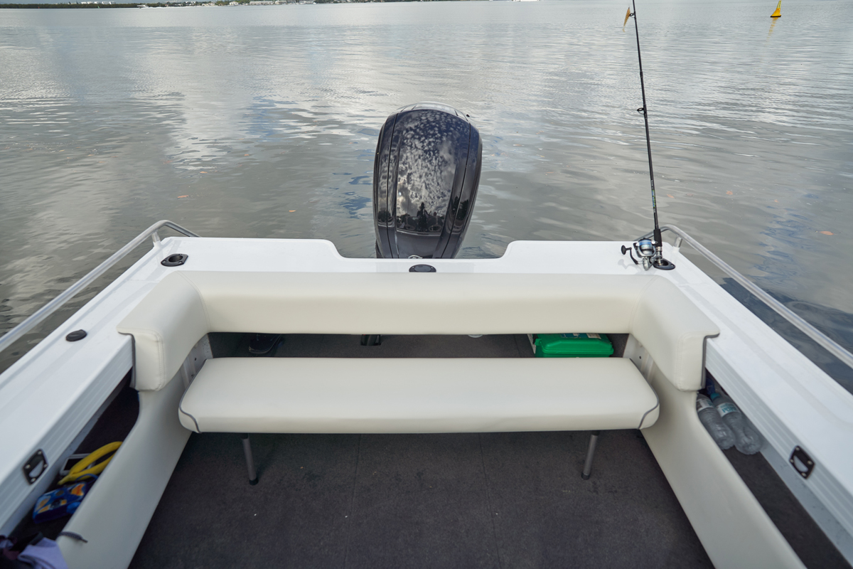 Rear view of a Quintrex boat's interior featuring a white upholstered bench seat, a fishing rod, and an outboard motor.