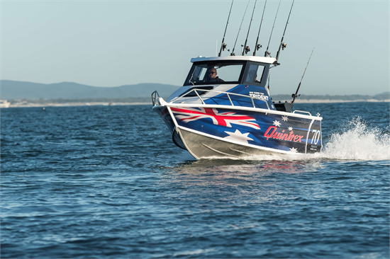A blue Quintrex Trident fishing boat with Australian flag graphics cruising across choppy blue water.